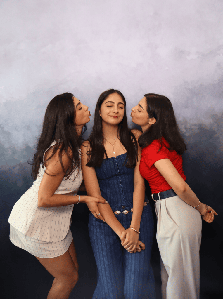 3 young women posing in front of a elegant photobooth backdrop both kissing the girl in the middle.
