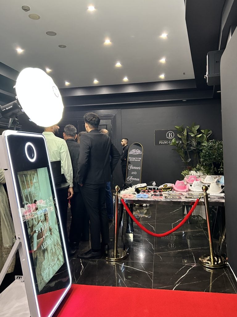 Mirror photobooth set up in Sydney Lidcombe with red carpet, gold bollards, props and a black backdrop. The photobooth screen is also customised with the couples photo and names.