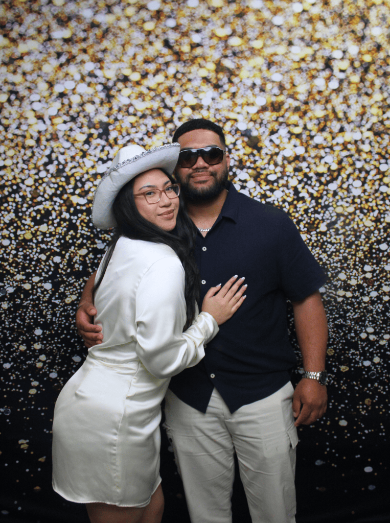 Couple posing for a photo booth photo with a gold backdrop.