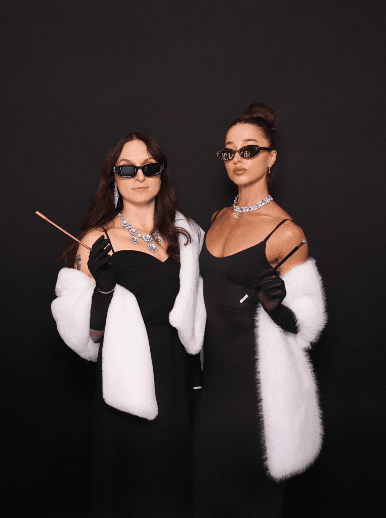 Black backdrop display, two women dressed in Hollywood themed outfits posing in front of photo booth.